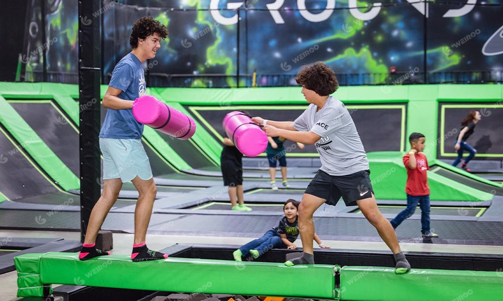 Gladiator battle beam game over foam pit, a classic trampoline park attraction.