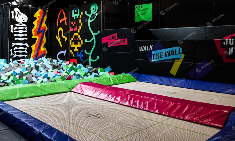 Professional trampoline with Walk the Wall feature, adjacent to a foam pit with a neon climbing wall above it.
