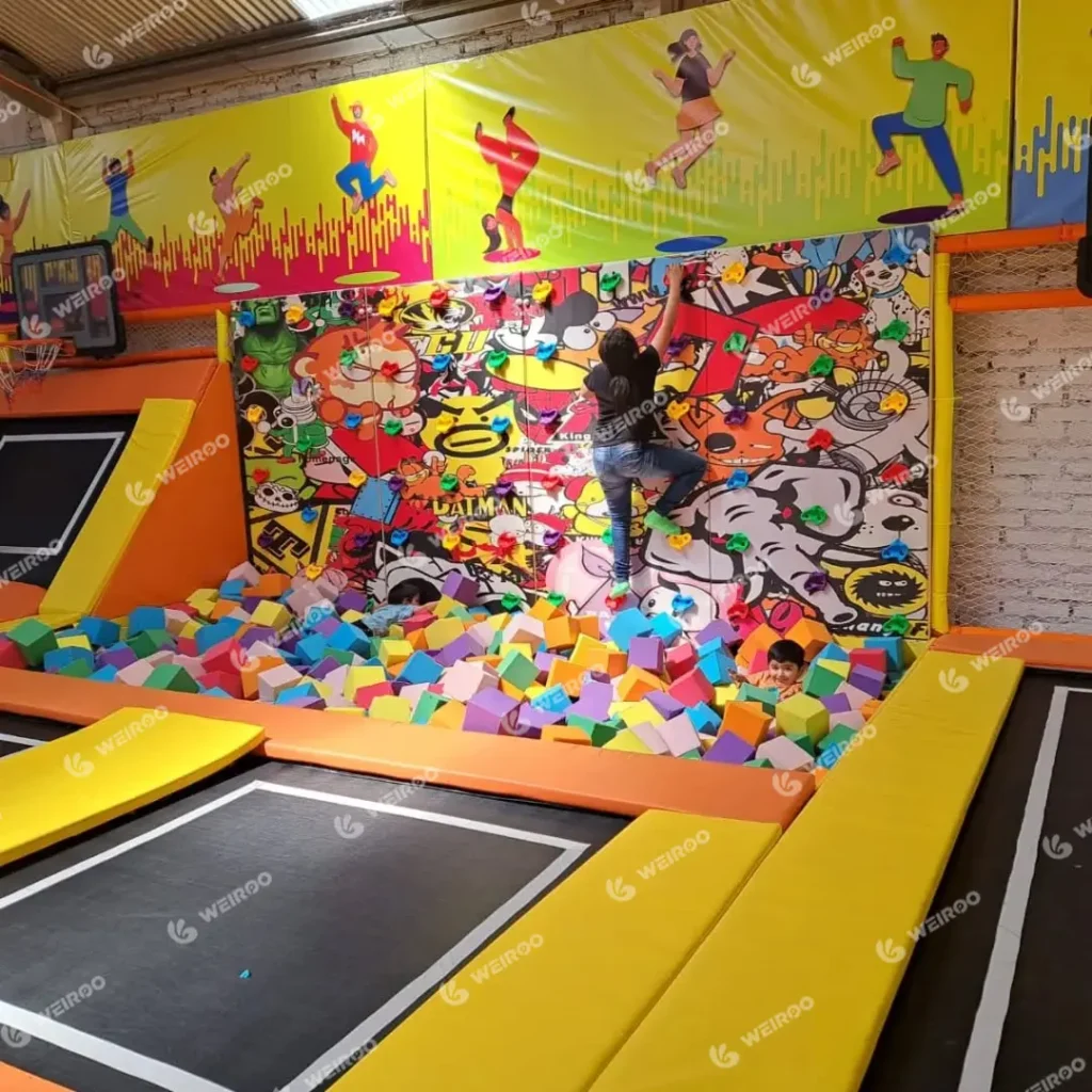 Interactive climbing wall with colorful graffiti art over a foam pit.