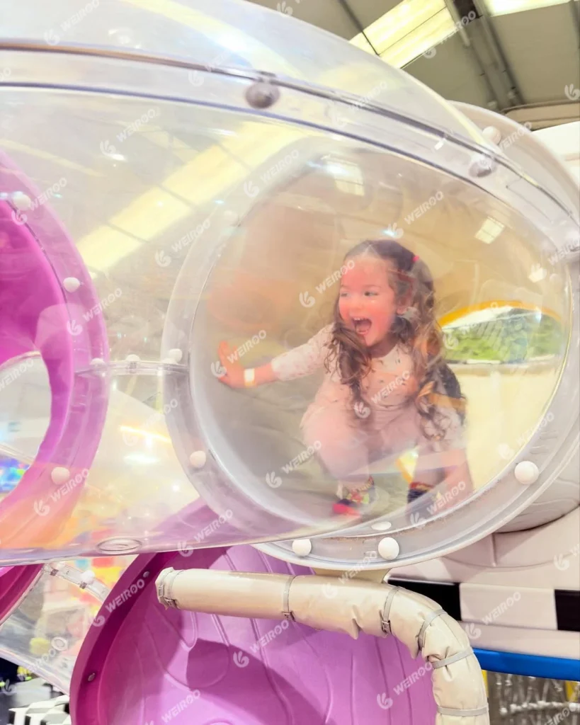 Child crawling through a transparent tube tunnel in the soft play structure.