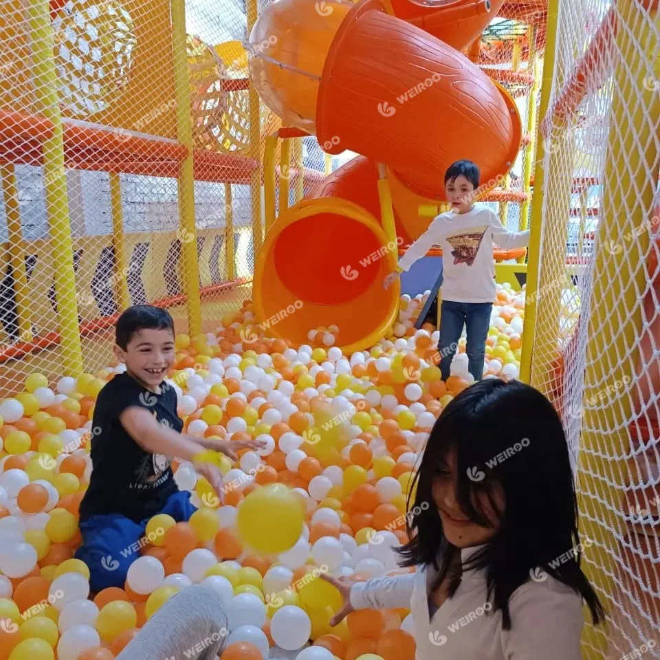 Kids throwing balls inside the multi-level indoor playground maze structure.