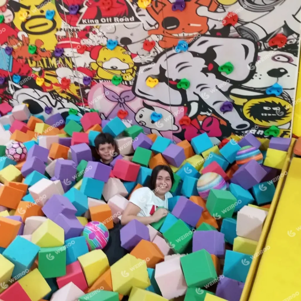 Wide view of the interactive climbing wall featuring cartoon character graffiti art above a large foam pit area at Happy Jump trampoline park in Chile.