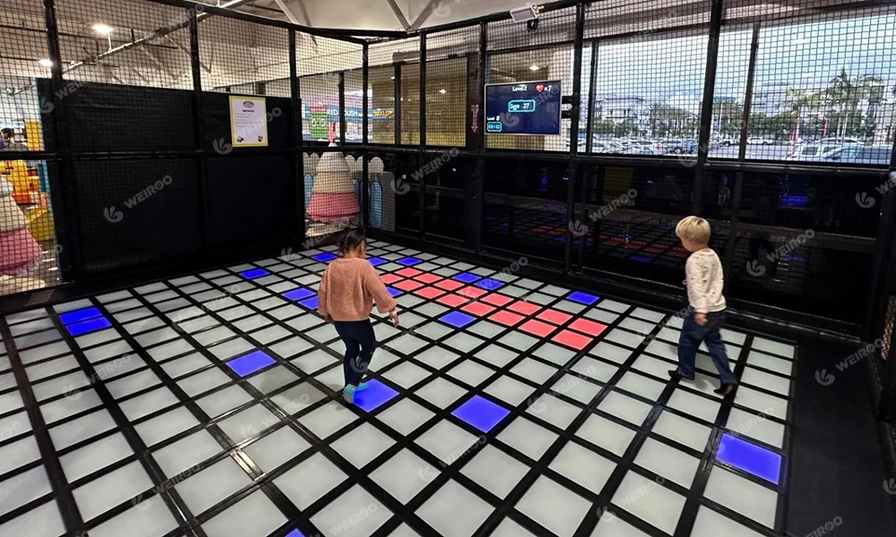 Kids playing on interactive LED floor grid game stepping tiles.