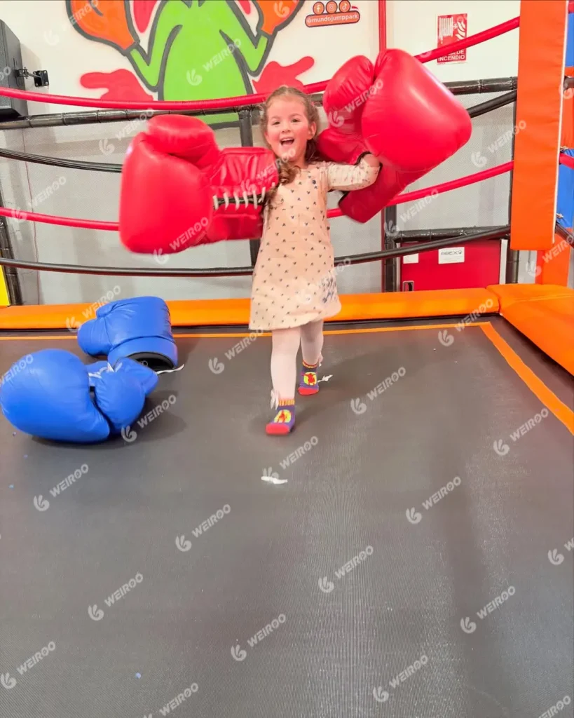 Little girl wearing giant foam boxing gloves in the trampoline park fighting zone.