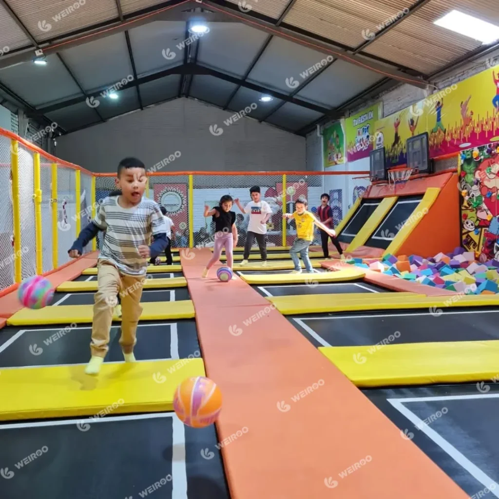 Action shot of kids jumping and playing ball on trampolines.
