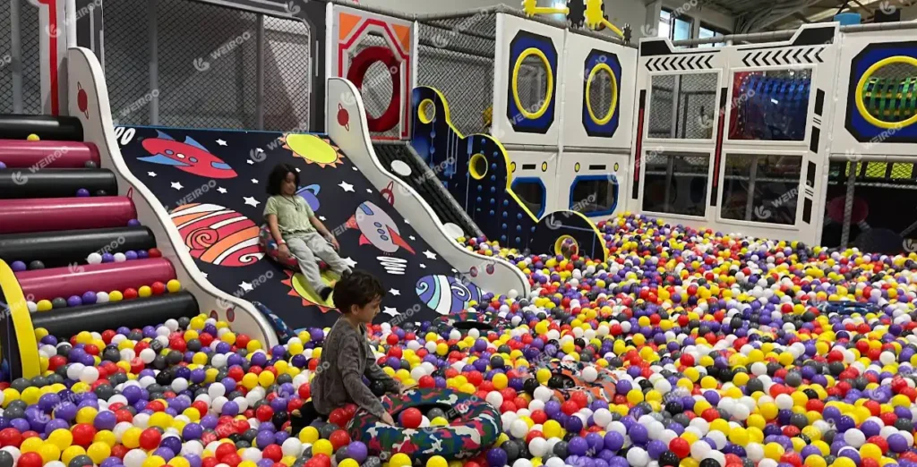 Multi-level space themed indoor playground with donut slide and large ball pit.