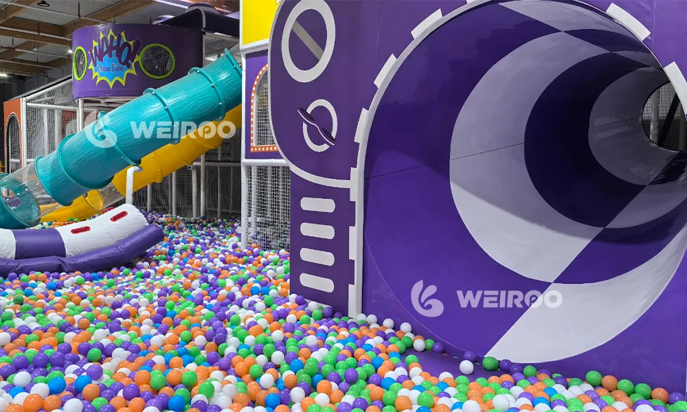 A vibrant indoor playground featuring a large ball pit and custom purple and teal tube slides, showcasing the professional design capabilities of Weiroo Play equipment manufacturer.
