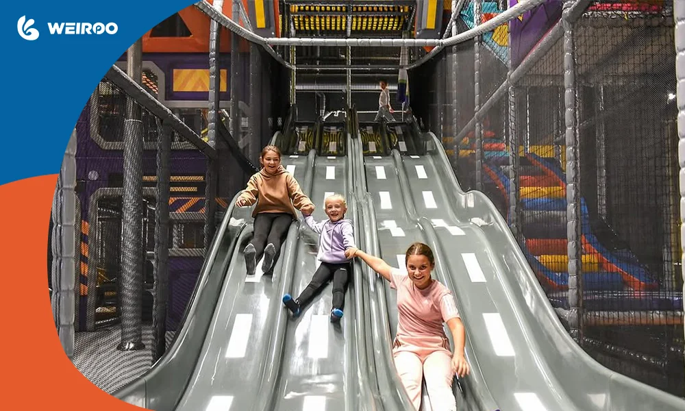 Happy children racing down a multi-lane slide with a road design in a commercial indoor playground.